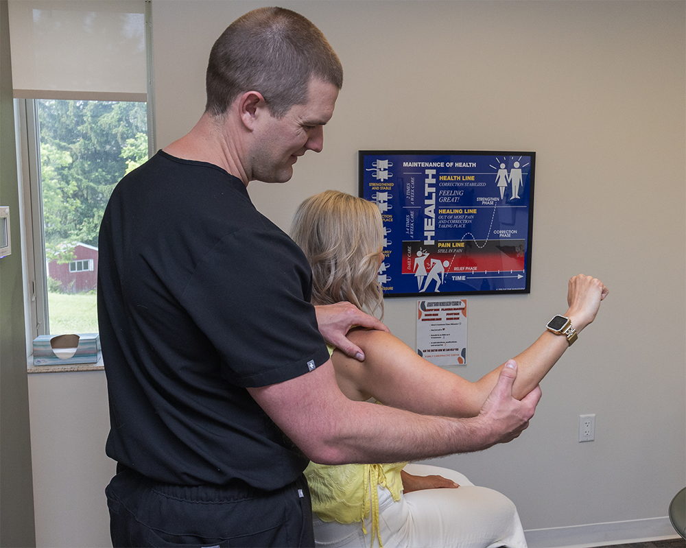 Dr. Kevin Hartung guiding an adult patient through a shoulder mobility evaluation in a clinical setting.