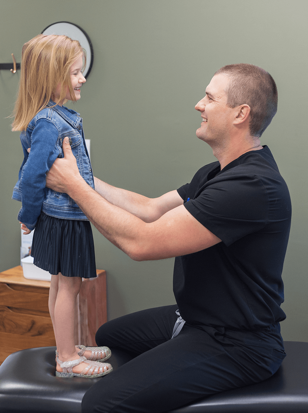 Dr. Kevin Hartung assisting a young child standing on a treatment table during a gentle posture or balance assessment.